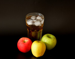 Tall glass of fruit juice mix with ice on black background, ripe apples of different varieties...