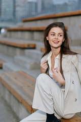 Businesswoman sitting on stairs, wearing stylish light-colored suit, expressing confidence and joy...