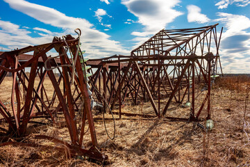 Old rusty transmission line support dumped in a field for dismantling, a pile of rusty iron and...