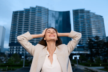 Confident businesswoman celebrating success outdoors in a modern urban setting with skyscrapers in...