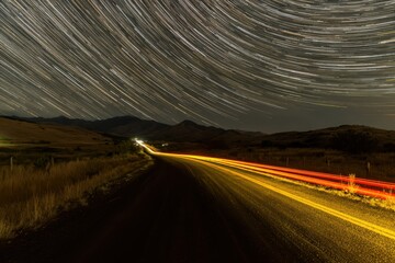 A captivating long exposure image of a car driving down a road at night, with streaks of light trailing behind it, creating a sense of motion and speed.