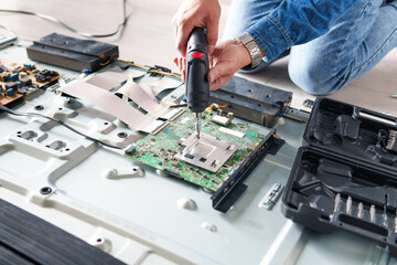 Technician repairing circuit board of a big led tv with an electric screwdriver