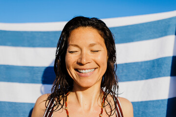 Happy woman smiling with eyes closed at beach with striped towel