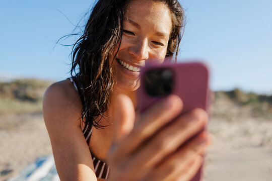 Smiling woman using smartphone on beach, enjoying summer vacation