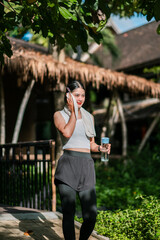 Woman in athletic wear with water bottle, enjoying a sunny day in a green park setting.