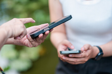 Two people interacting with smartphones in an outdoor setting, focusing on hands and devices.