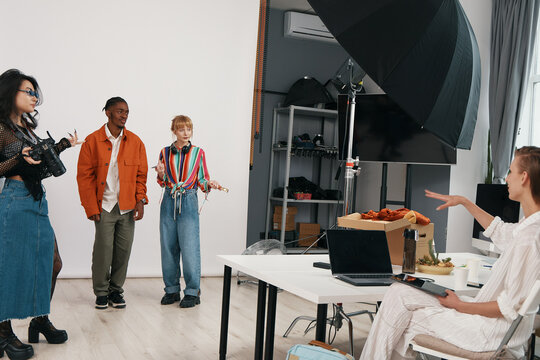 Young adult woman directing colleagues and coworkers in a modern workplace, socializing and collaborating on a business project with Gen Z professionals.