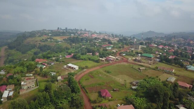 Drone aerial of Kapchorwa in Eastern Uganda showing red dirt roads, dispersed houses, farmlands and lush green slopes of Mount Elgon under soft daylight.