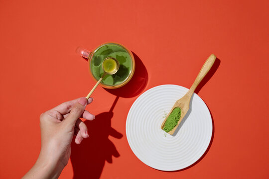A hand prepares a soothing matcha tea on a organce background
