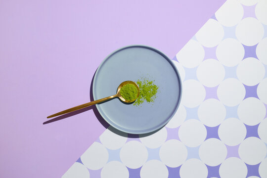 An artistic flatlay of matcha powder on a plate with a golden spoon