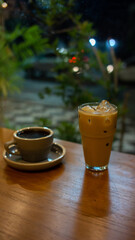 A cup of hot coffee and a glass of ice latte on wooden table with blurred outdoor traffic background