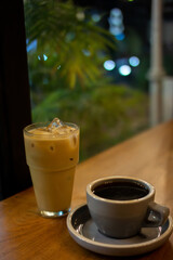 A cup of hot coffee and a glass of ice latte on wooden table with blurred green foliage background