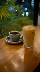 A cup of hot coffee and a glass of ice latte on wooden table with blurred green foliage background