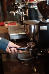 A person is holding a portafilter beneath a coffee grinder. The grinder s dispenser releases freshly ground coffee into the portafilter