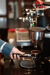 A person is holding a portafilter beneath a coffee grinder. The grinder s dispenser releases...