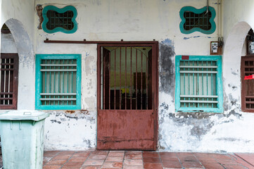 Rusty red door with teal windows in aged colonial wall
