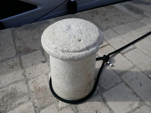 Concrete mooring bollard on shipping dock with ropes tied