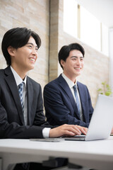 デスクでお客様に説明する若手の営業マン複数のイメージ　ミーティングや打ち合わせなど 縦