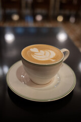A cup of coffee latte with froth art on the table with blurred background lights
