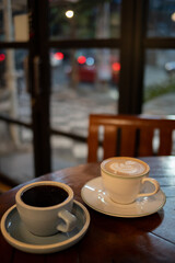 A cup of hot black coffee and hot latte with froth art on the table with blurred traffic background