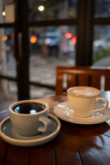 A cup of hot black coffee and hot latte with froth art on the table with blurred traffic background