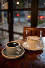 A cup of hot black coffee and hot latte with froth art on the table with blurred traffic background