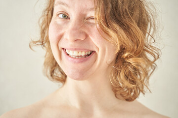 Smiling caucasian adult female with curly hair winking at camera in bright natural light.