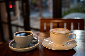 A cup of hot black coffee and hot latte with froth art on the table with blurred traffic background