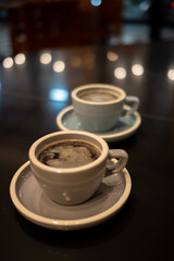 Two ceramic cups filled with steaming black coffee are placed on saucers atop a glossy, reflective table surface
