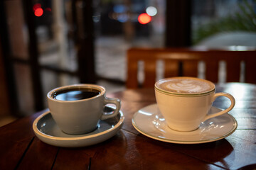 A cup of hot black coffee and hot latte with froth art on the table with blurred traffic background