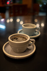 Two ceramic cups filled with steaming black coffee are placed on saucers atop a glossy, reflective table surface