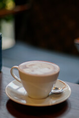 A white ceramic cup filled with a frothy beverage sits on a matching saucer, placed on a dark wooden table