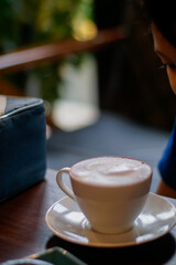 A white ceramic cup filled with a frothy beverage sits on a matching saucer, placed on a dark...