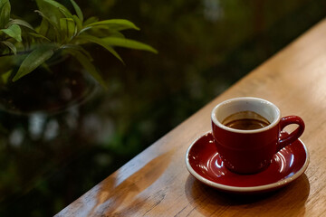A red cup of coffee on wooden table with blurred green background