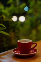 Espresso in a red cup on wooden table with blurred green background