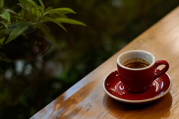 Espresso in a red cup on wooden table with blurred green background