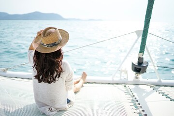 A lady with long hair wearing hat sitting on a luxurious white yacht facing beautiful sunset and sea