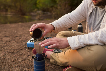 Coffee filtering process. Man making coffee for breakfast outdoors early in the morning by a creek,...