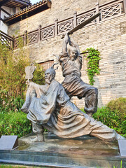 A dynamic bronze statue of two ancient warriors in action, one kneeling with a fan, one mid-strike...