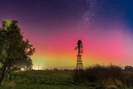 Aurora Australis and the Milky Way in the sky above a farm windmill