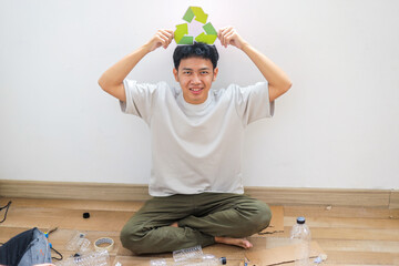 Fototapeta premium Happy Young Asian Man Holding Recycling Symbol Over His Head While Sitting On The Floor