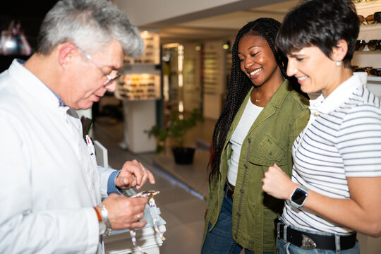 Optician showing eyeglasses to two women in optical store