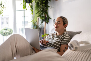 Young woman working from home laying on bed using laptop