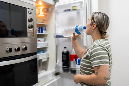 Woman drinking fresh water directly from the bottle in the kitchen