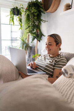 Young woman working from home is using laptop in bed smiling