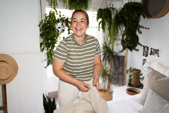 Woman making bed in cozy green bedroom with houseplants