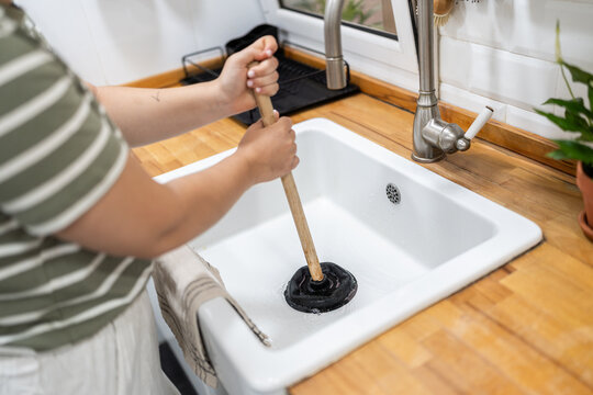 Woman using plunger to unclog kitchen sink drain