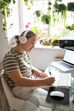 Young woman wearing headphones taking notes while working