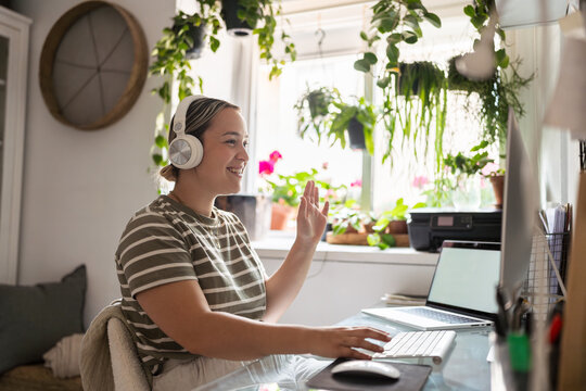 Young woman working from home having a video call waving