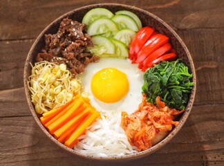 Bibimbap is a Korean dish in the form of a bowl of white rice topped with side dishes of vegetables, beef, eggs and spicy gochujang sauce.